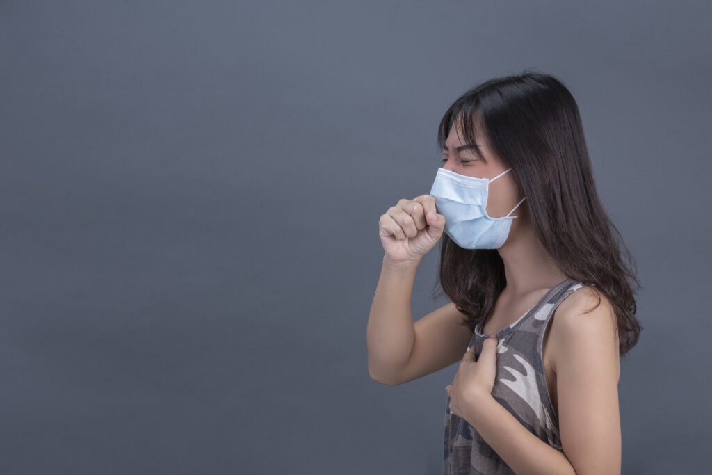 Young girl is wearing mask while coughing on black background.